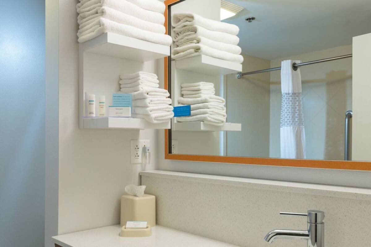 A bathroom with a sink, mirror, towel rack, and shelves with folded towels.
