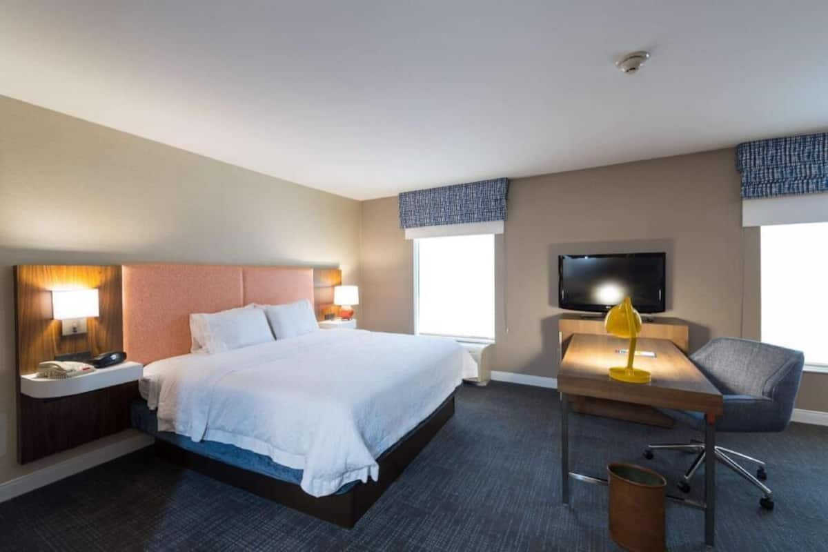 Ett hotellrum med en säng, sängbord, ett skrivbord med en stol, en tv och fönster.