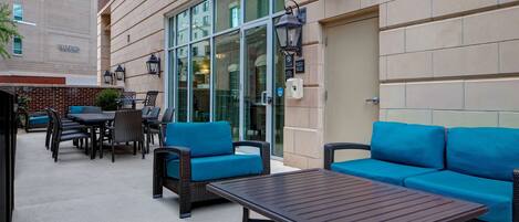 An outdoor patio with blue sofas and a table, a brick building in the background, and a glass door entrance.
