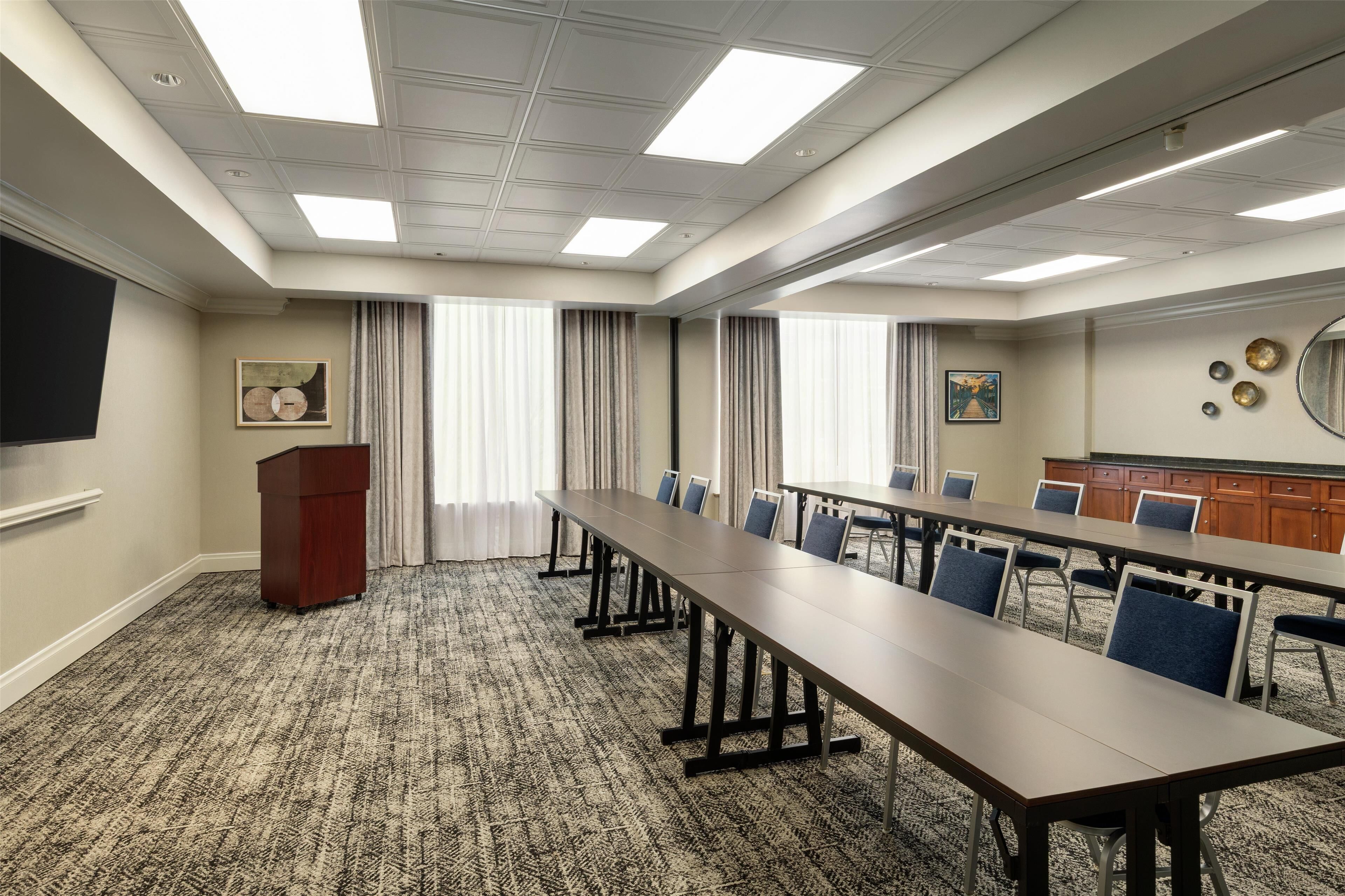 A conference room with a long table, chairs, a podium, and a large screen.