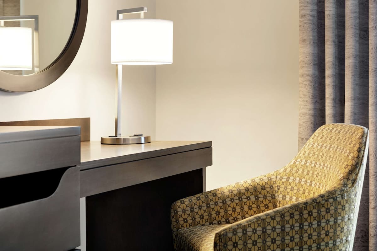 Ein Hotelzimmer mit Schreibtisch, Stuhl, Lampe und einem großen Spiegel.