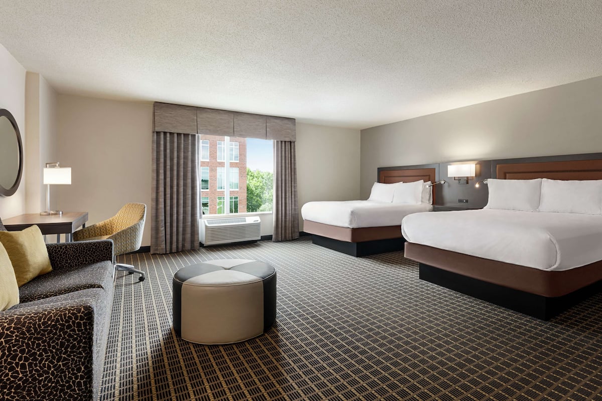 Ein Hotelzimmer mit zwei Betten, einem Schlafsofa, einem Sessel und einem kleinen Hocker.