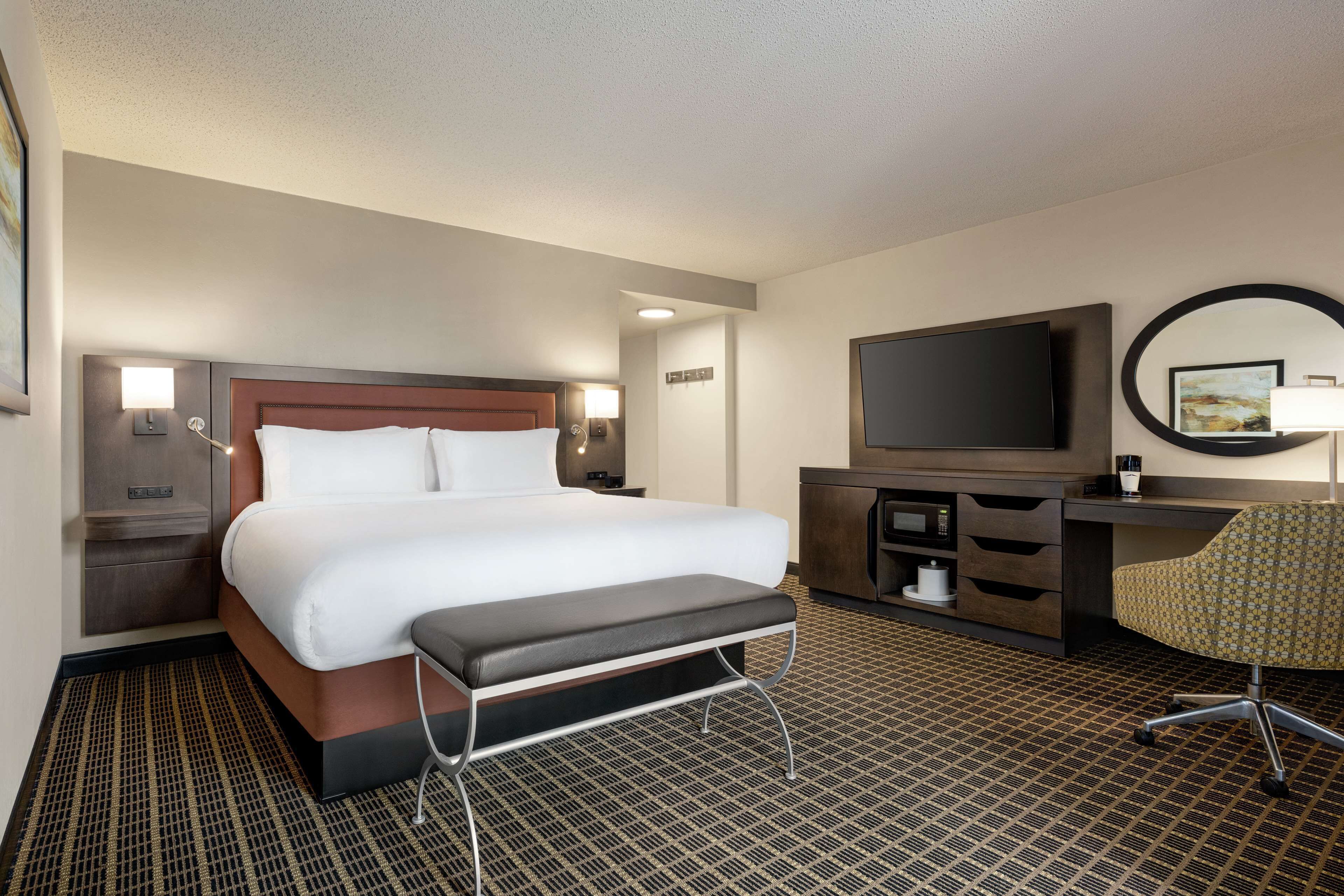 Une chambre d’hôtel avec un grand lit, un bureau avec une chaise, une télévision et un miroir.