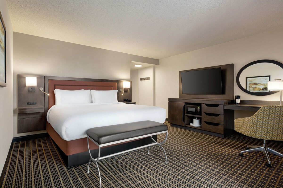 Une chambre d’hôtel avec un grand lit, un bureau avec une chaise, une télévision et un miroir.