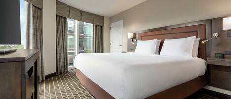 A hotel room with a large bed, a desk, a TV, and a view of the city.