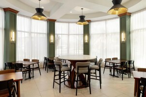 Un comedor amplio con mesas y sillas redondas, ventanas grandes con cortinas traslúcidas e iluminación colgante.