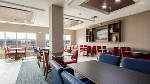 A modern hotel dining area with multiple tables and chairs, large windows offering a view of the outdoors, and a flat-screen TV mounted on the wall. - Holiday Inn Express & Suites Lenoir Cty by IHG (Lenoir City)