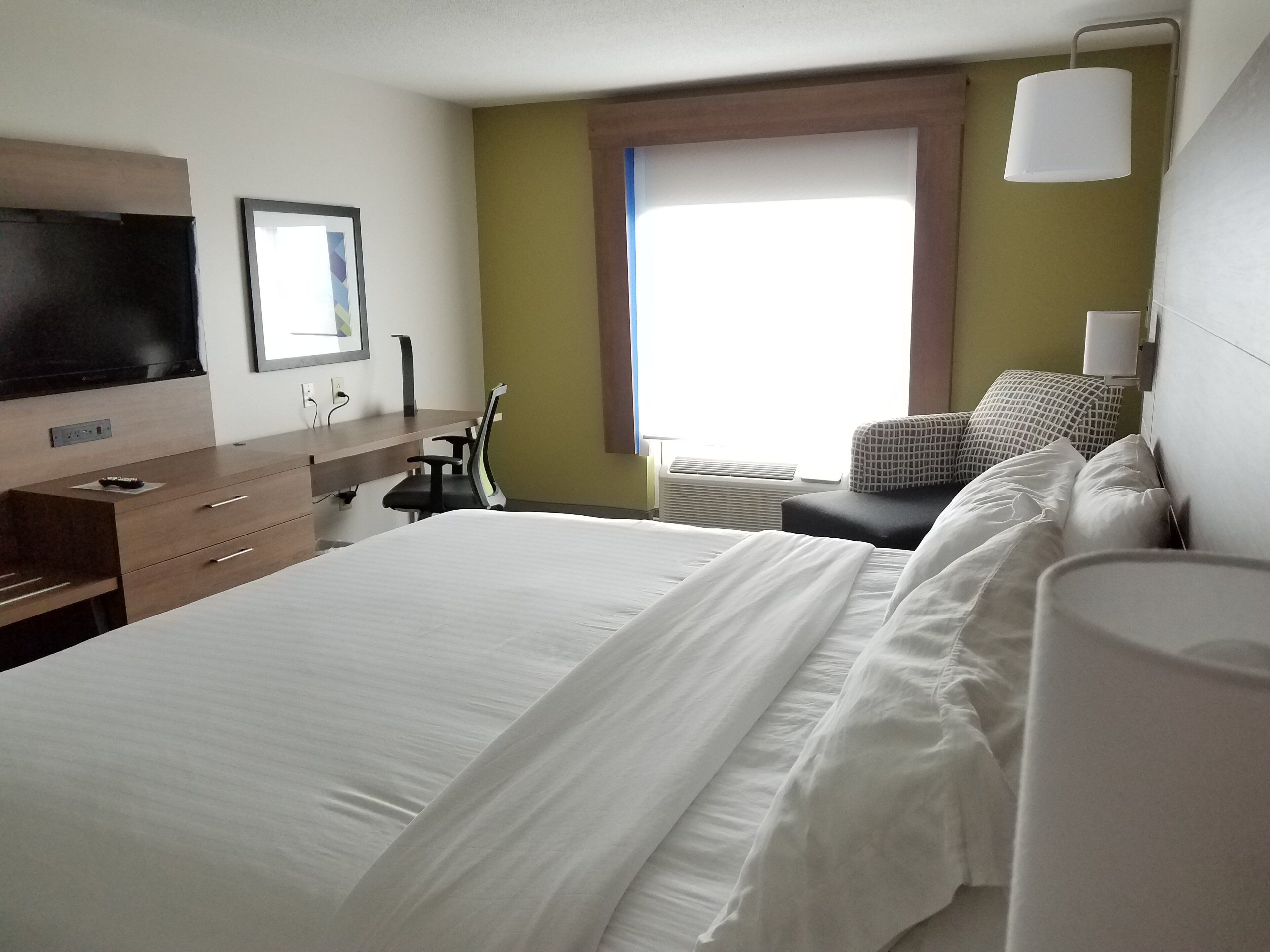 A hotel room with a bed, a desk, a chair, a television, and a window.