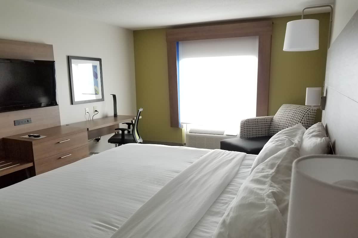 A hotel room with a large bed, a desk with a chair, a flat-screen TV, and a window with a view.