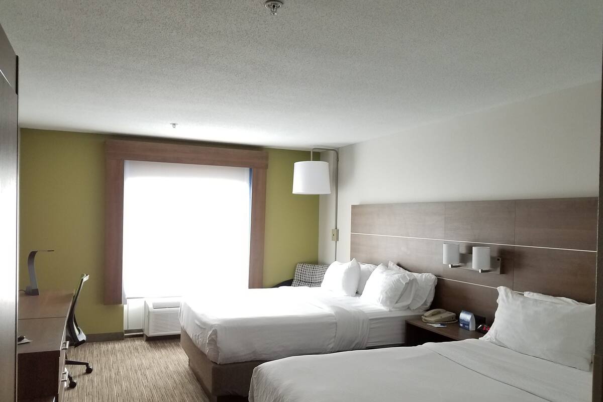 A hotel room with two beds, a desk, a lamp, and a window.