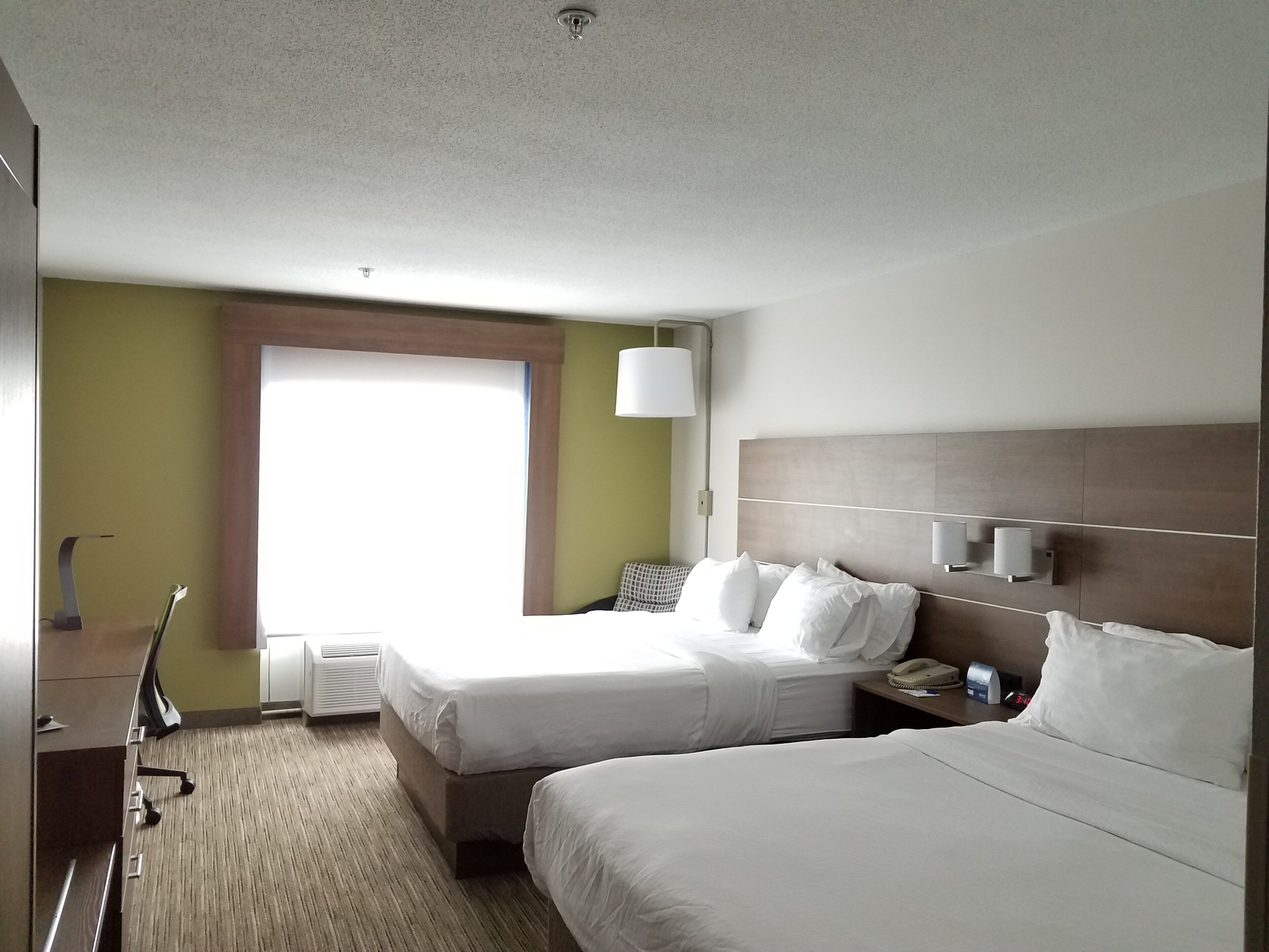 A hotel room with two beds, a desk, a lamp, and a window.