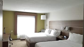 A hotel room with two beds, a desk, a lamp, and a window.