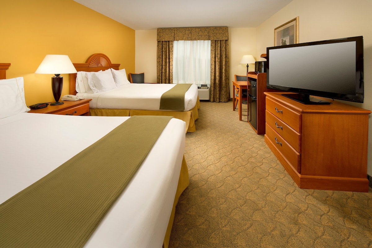 A hotel room with two beds, a television, a desk with a chair, and a dresser.