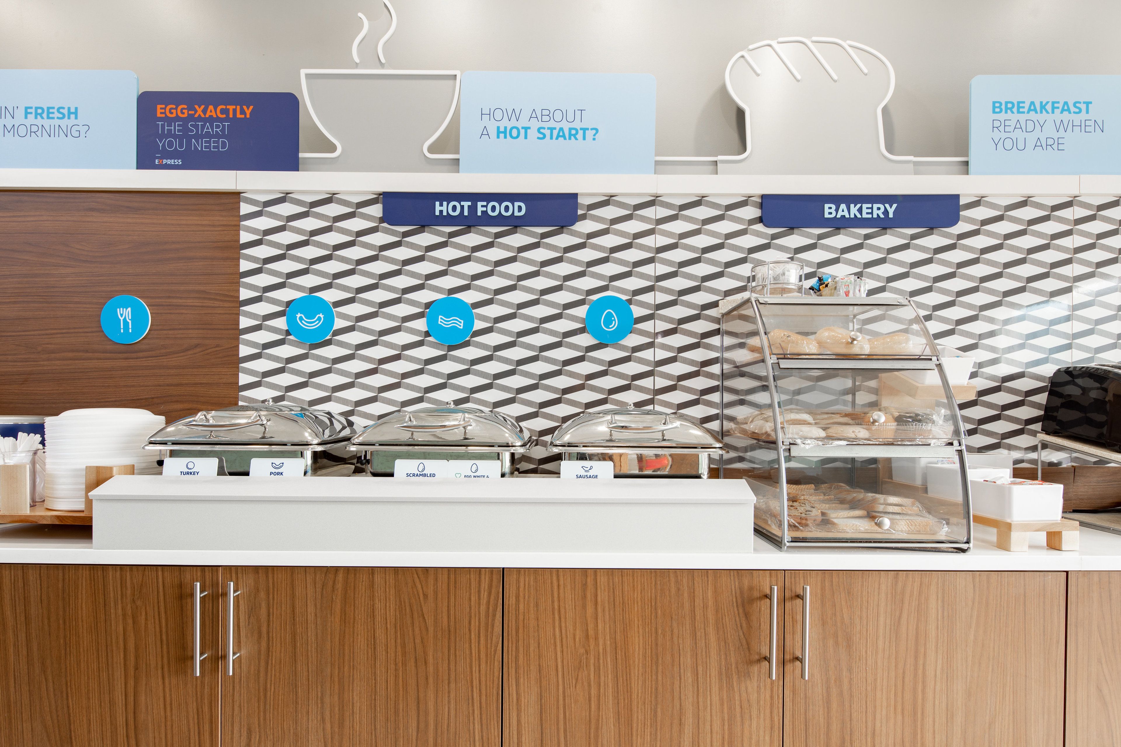 Zona de desayuno tipo buffet con alimentos calientes y panadería, que incluye opciones como pavo, cerdo, huevos revueltos y salchichas.