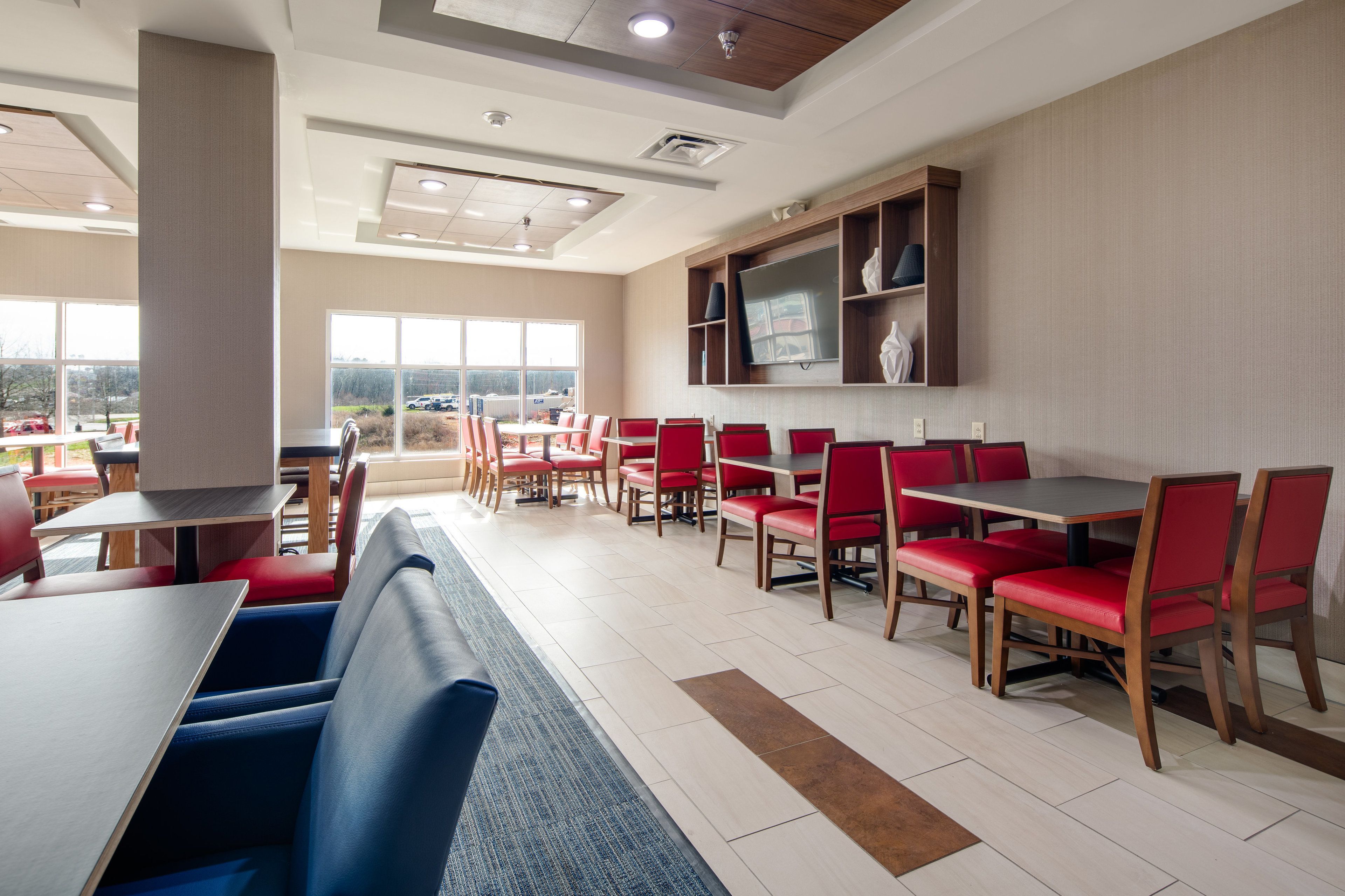 A modern restaurant with red and blue seating, large windows, and a flat-screen TV on the wall.