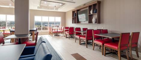 A modern restaurant with red and blue seating, large windows, and a flat-screen TV on the wall.