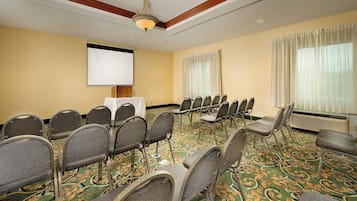 A conference room with a projector screen, rows of chairs, a carpeted floor, and a ceiling fan.