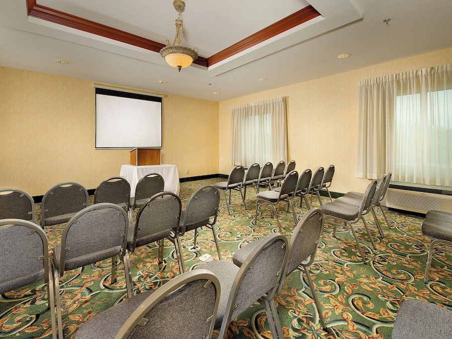 A conference room with a projector screen, rows of chairs, a carpeted floor, and a ceiling fan.