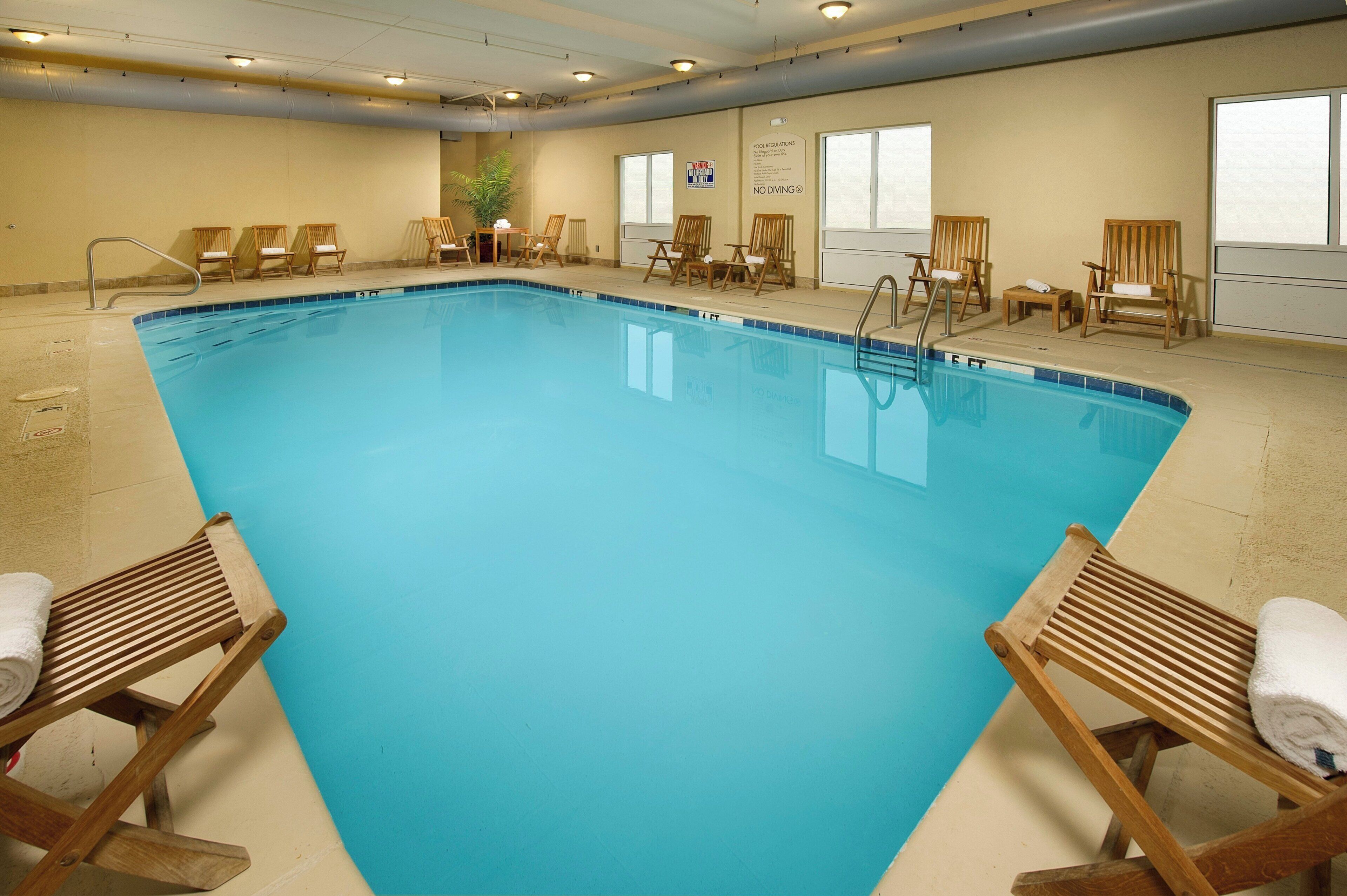 A large indoor swimming pool with multiple lounge chairs and a sign indicating pool regulations.