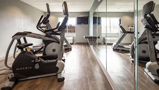 A gym with stationary bikes and treadmills, a large mirror, and a window with a view of trees. - Holiday Inn Express & Suites Lenoir Cty by IHG (Lenoir City)