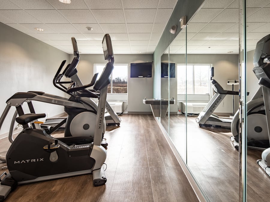 A gym with stationary bikes and treadmills, a large mirror, and a window with a view of trees.