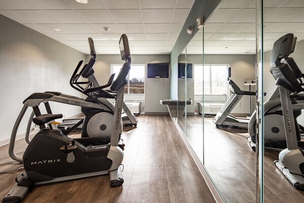 A gym with stationary bikes and treadmills, a large mirror, and a window with a view of trees. - Holiday Inn Express & Suites Lenoir Cty by IHG (Lenoir City)