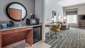 A hotel room with a kitchenette, a desk, a chair, a sofa, a TV, and a large window. - Hampton Inn & Suites-Dallas Allen (Allen)