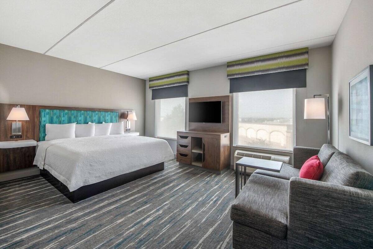 A hotel room with a bed, a desk, a TV, a sofa, and a window with a view.