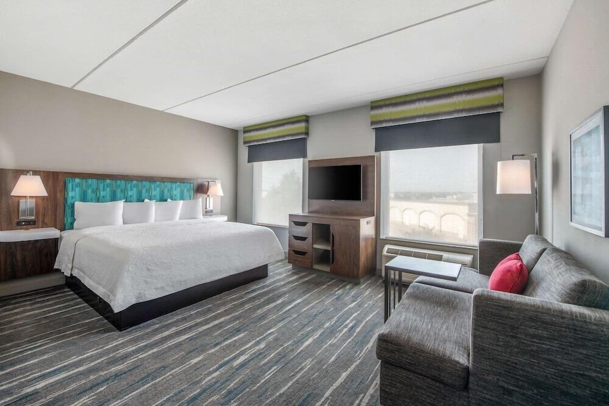 Quarto de hotel com cama, escrivaninha, televisão, sofá e janela com vista.