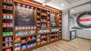 A snack shop with shelves stocked with various snacks and drinks, a chalkboard sign welcoming visitors, and a wall with a large 'Treats' sign. - Hampton Inn & Suites-Dallas Allen (Allen)