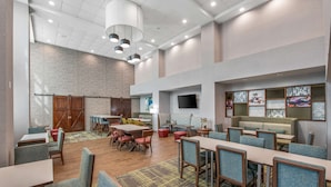 A spacious indoor area with multiple seating arrangements, including tables and chairs, a television mounted on the wall, and a patterned carpet. - Hampton Inn & Suites-Dallas Allen (Allen)