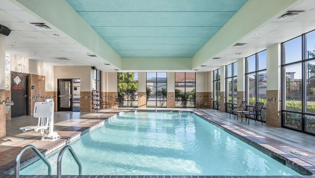 An indoor swimming pool with clear glass walls, a tiled floor, and a ceiling painted in a light teal color. - Hampton Inn & Suites-Dallas Allen (Allen)