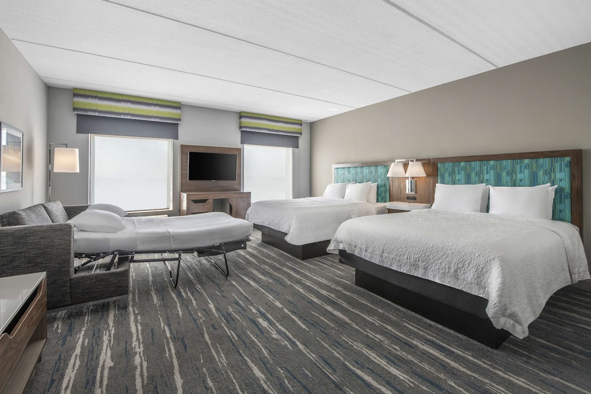 A hotel room with two beds, a sofa, a TV, and a desk.