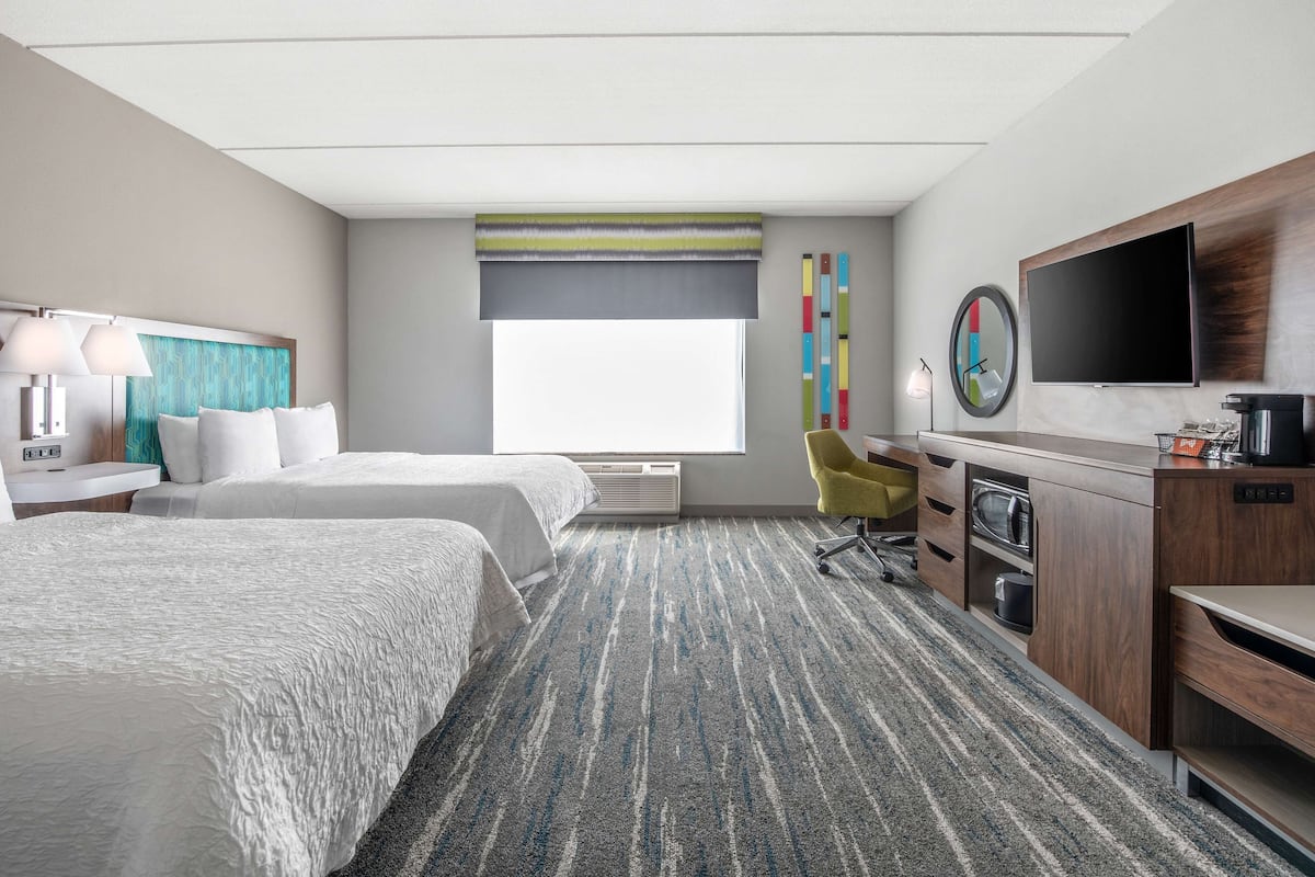 A hotel room with two beds, a desk, a TV, and a large window.