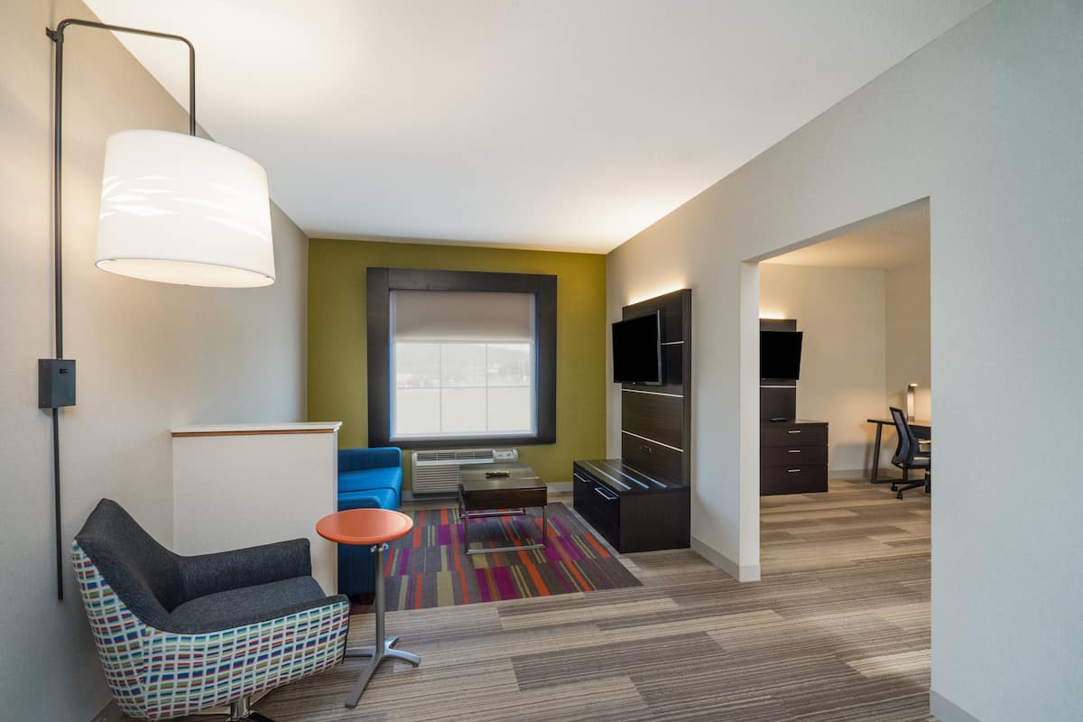 Una habitación de hotel moderna con un ventanal grande, un sofá, una silla, un escritorio y un armario.