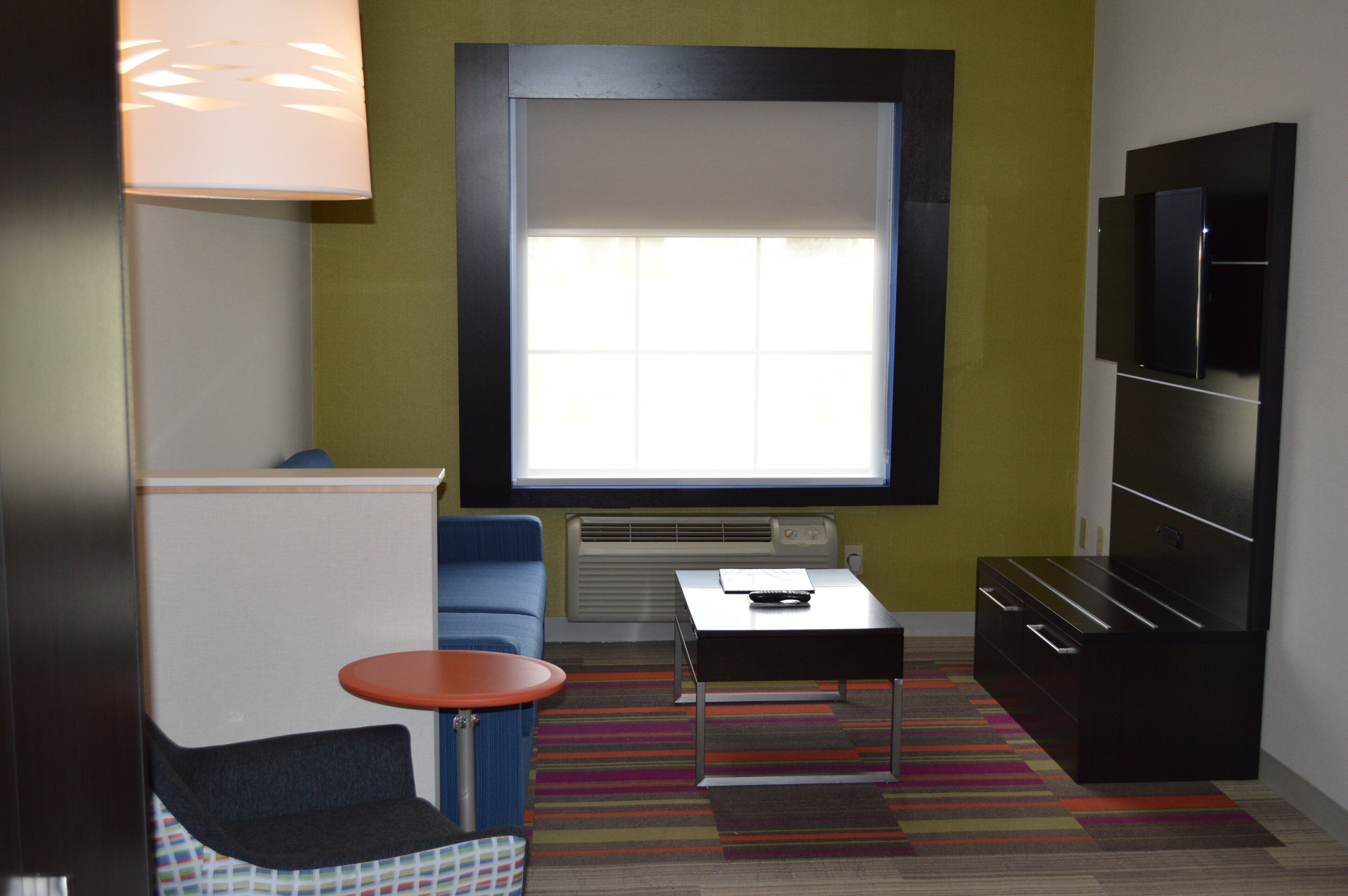 A compact room with a window, a television, a small table, a chair, and a sofa.