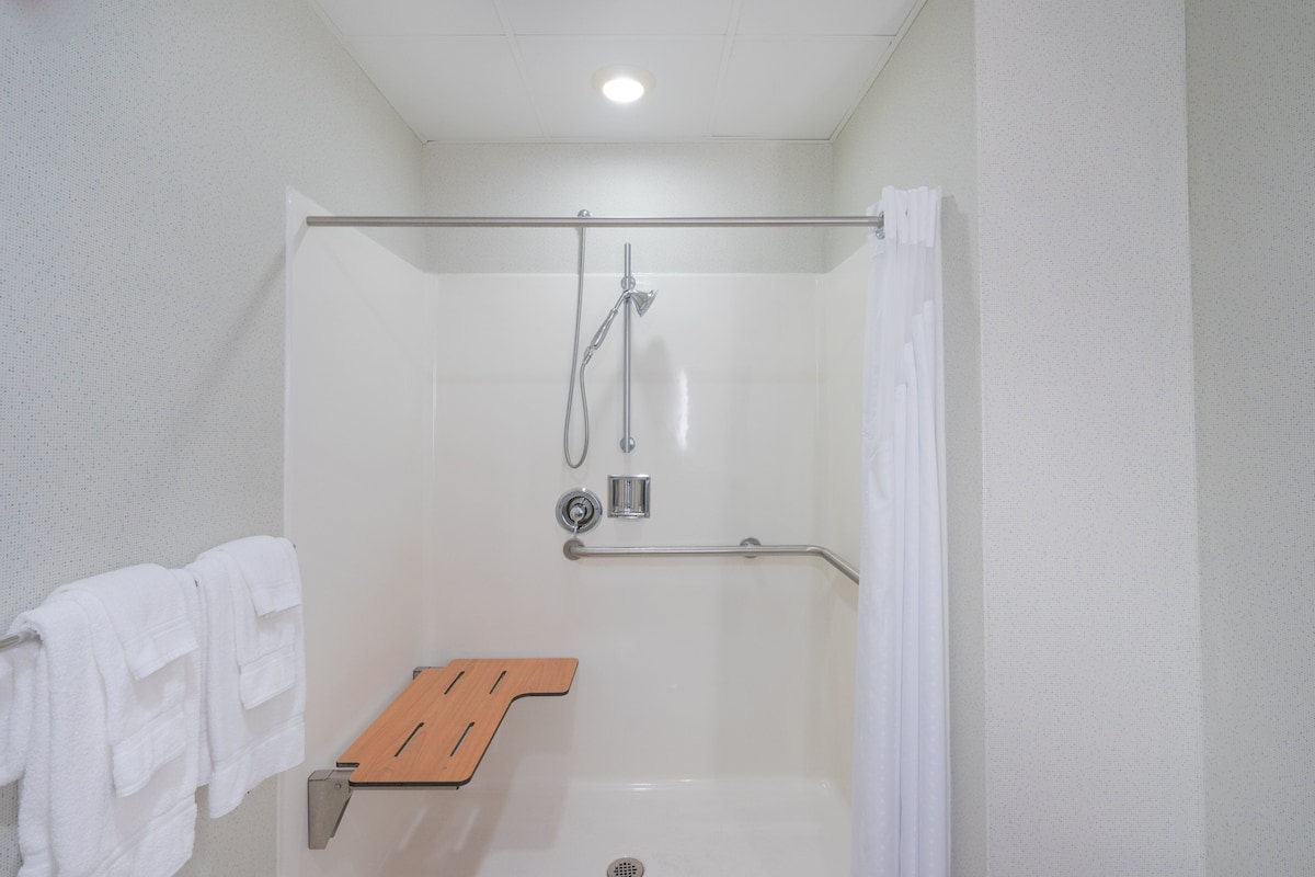 Ducha con puerta de vidrio, repisa de madera y toallero blanco.