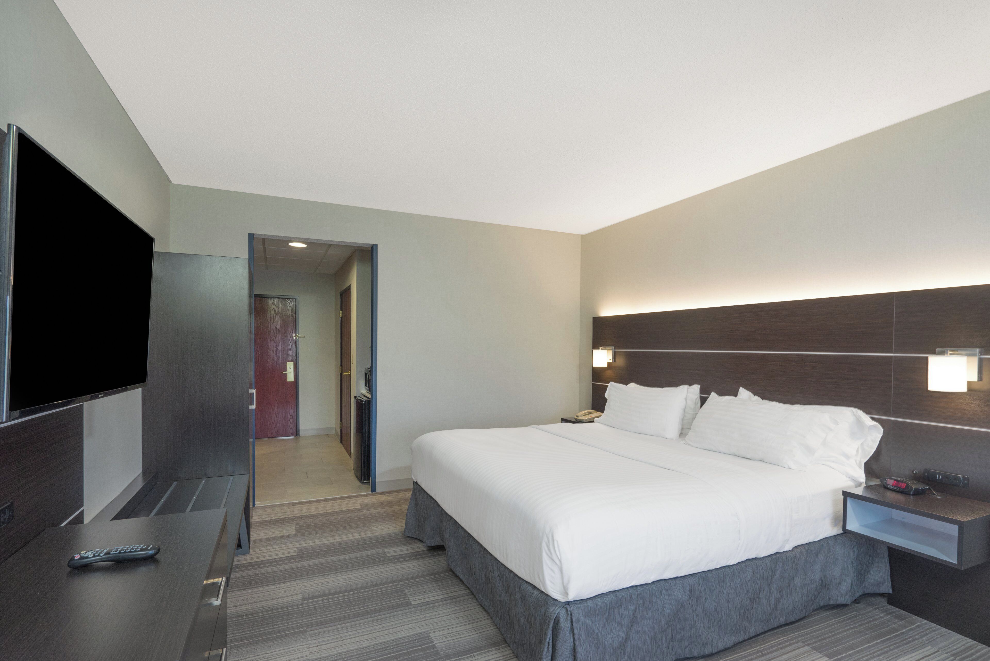 A hotel room with a large bed, a flat-screen TV, a bedside table, and a nightstand.
