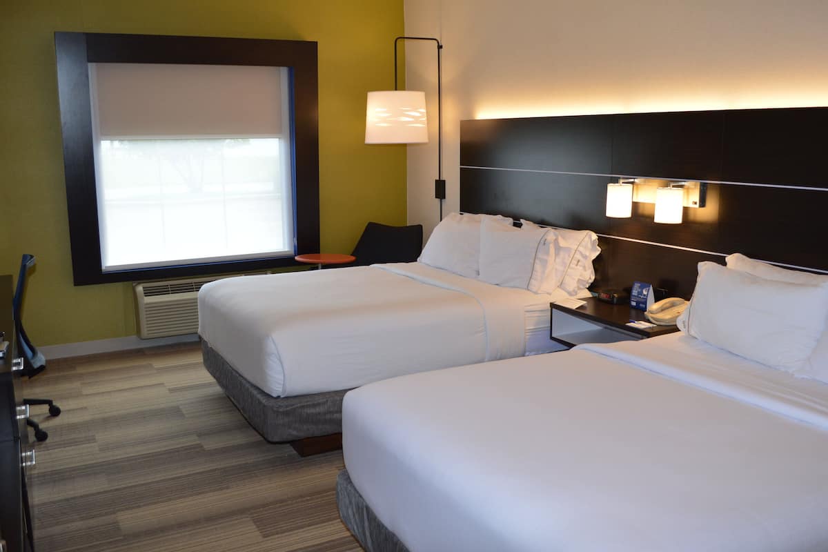 Una habitación de hotel con dos camas, un escritorio, una silla, una lámpara y una ventana.