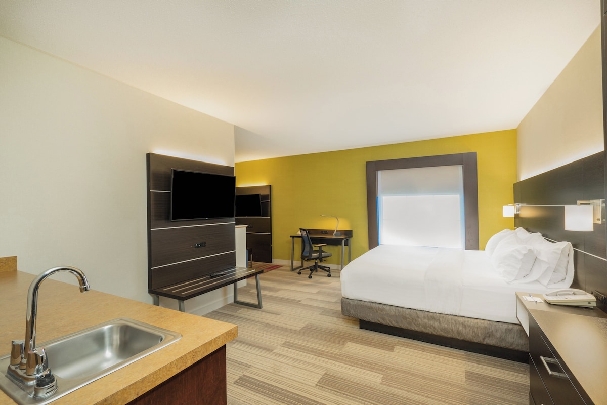 A hotel room with a bed, a desk, a TV, a sink, and a window.