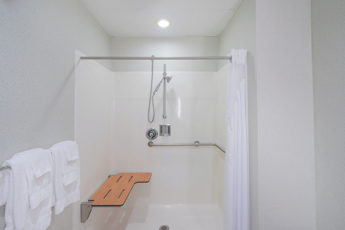 A shower with a glass door, a wooden shelf, and a white towel rack.