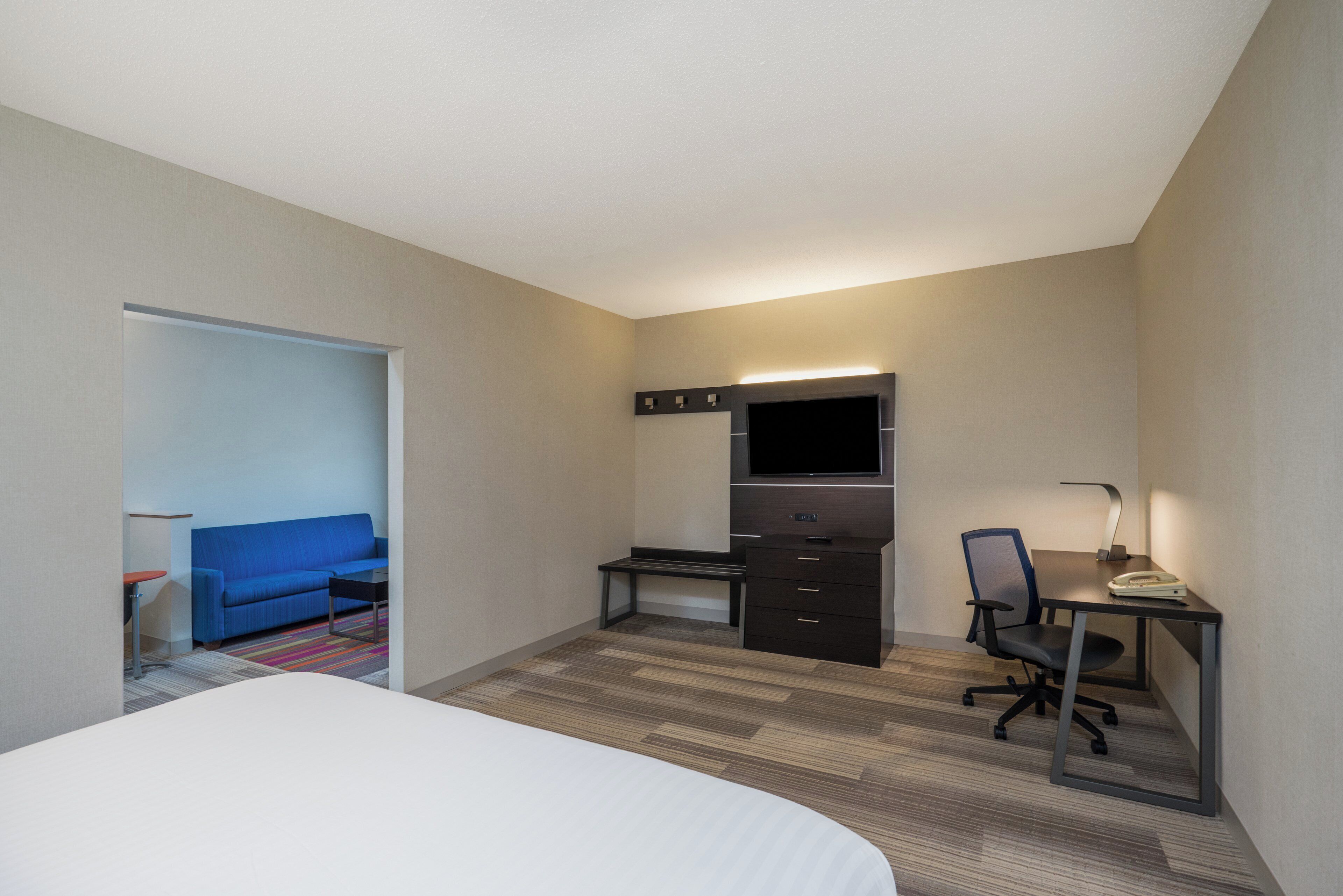 A hotel room with a bed, a desk with a chair, a television, and a small seating area with a sofa and a table.