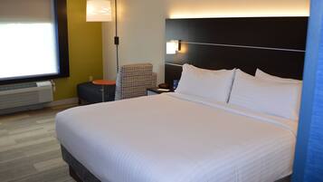 A hotel room with a large bed, a nightstand, a chair, a lamp, and a window with blinds.