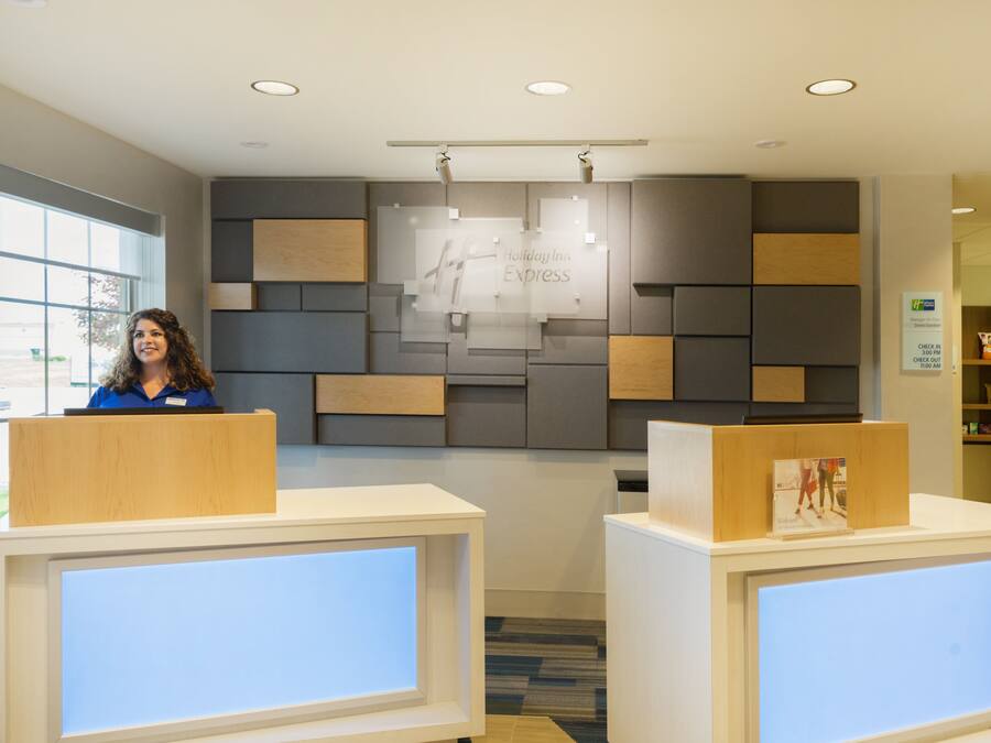 A reception area with a modern design, featuring a large glass display with the Holiday Inn Express logo, a reception desk, and a check-in counter.