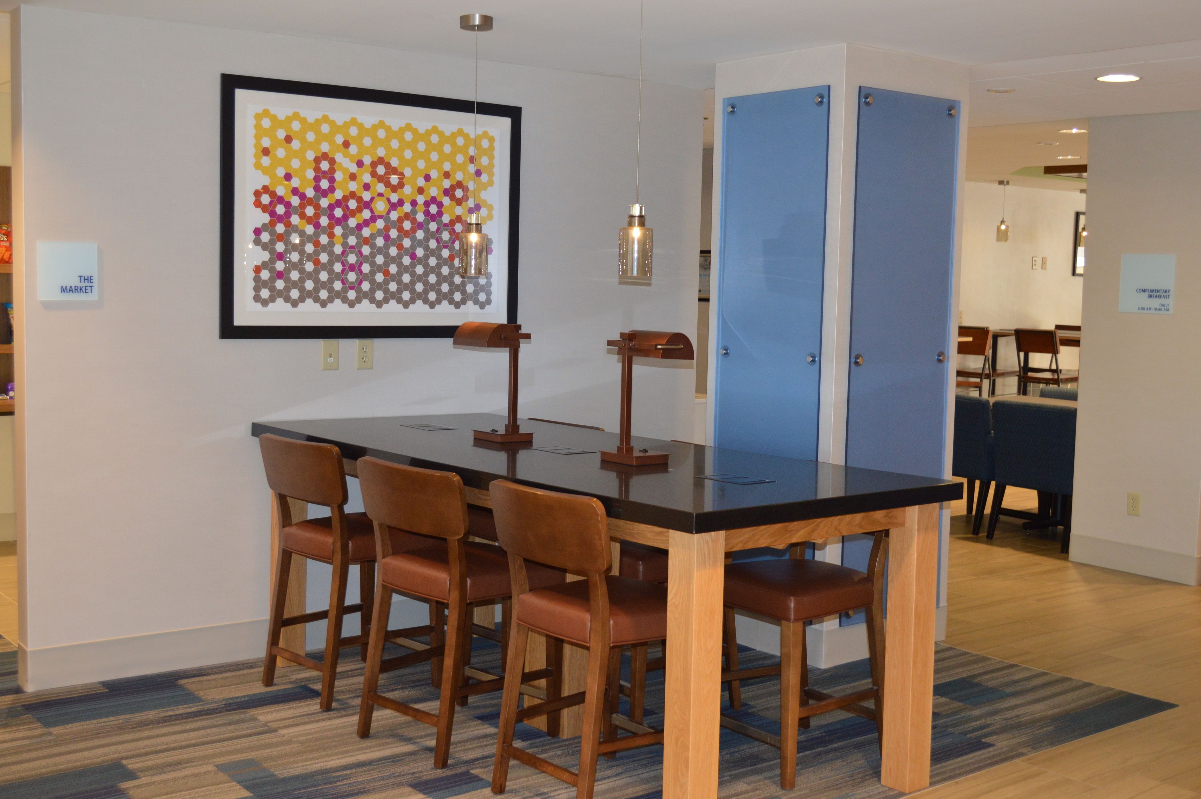 A modern dining area with a black table and wooden chairs, a colorful hexagonal wall art, and a blue partition.