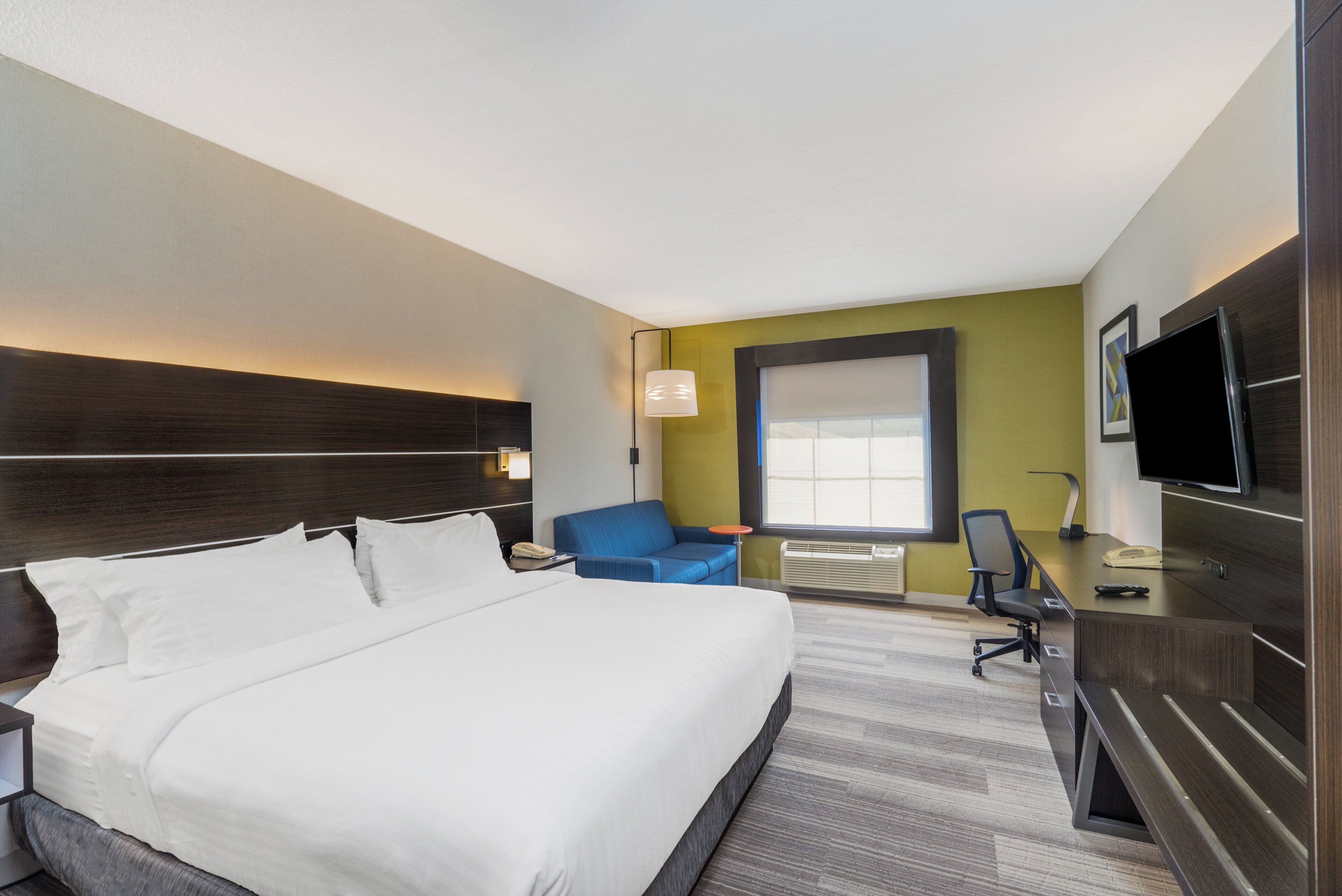 A hotel room with a large bed, a desk, a chair, a television, and a window.