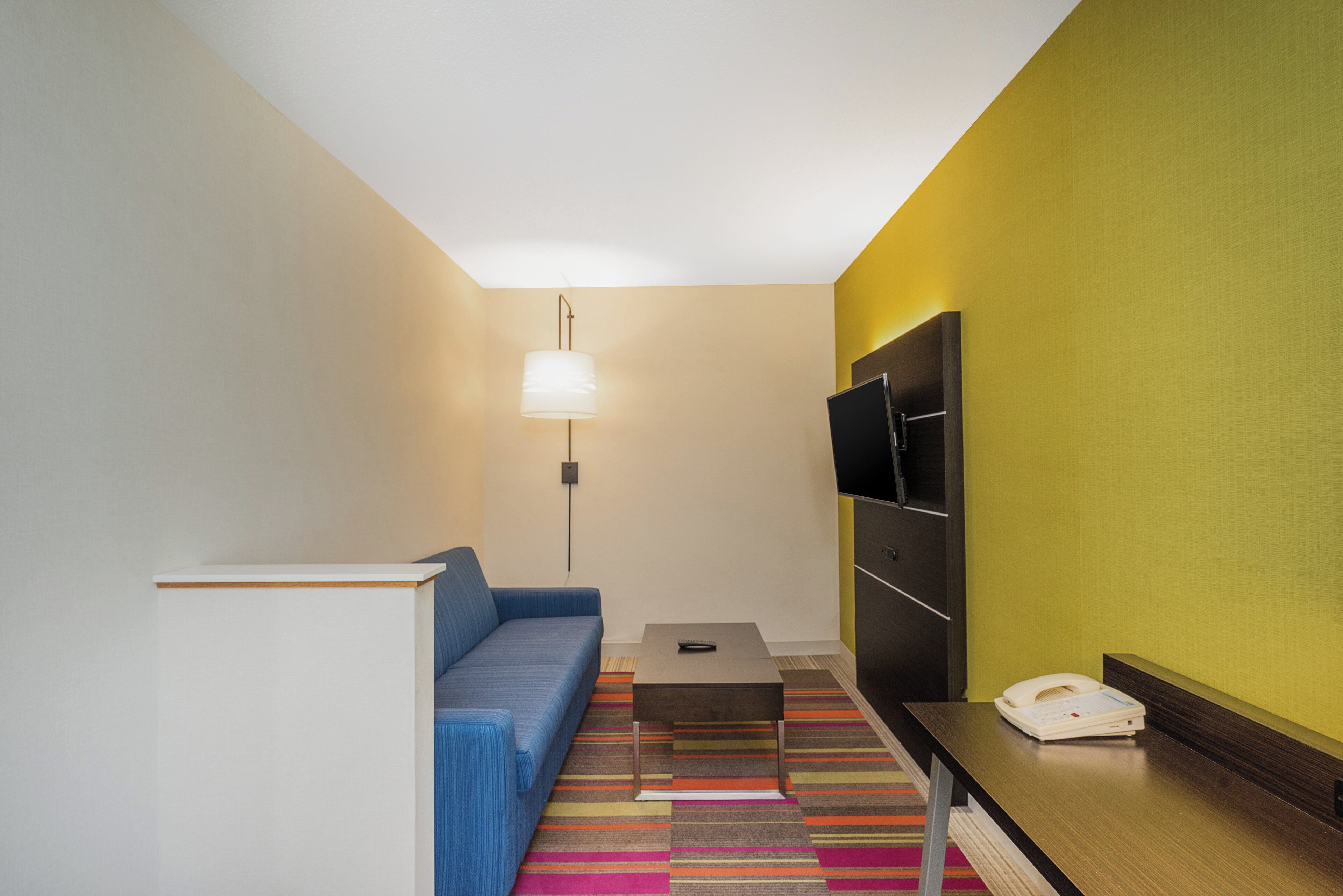 A hotel room with a sofa, a small table, a telephone, and a TV mounted on the wall.