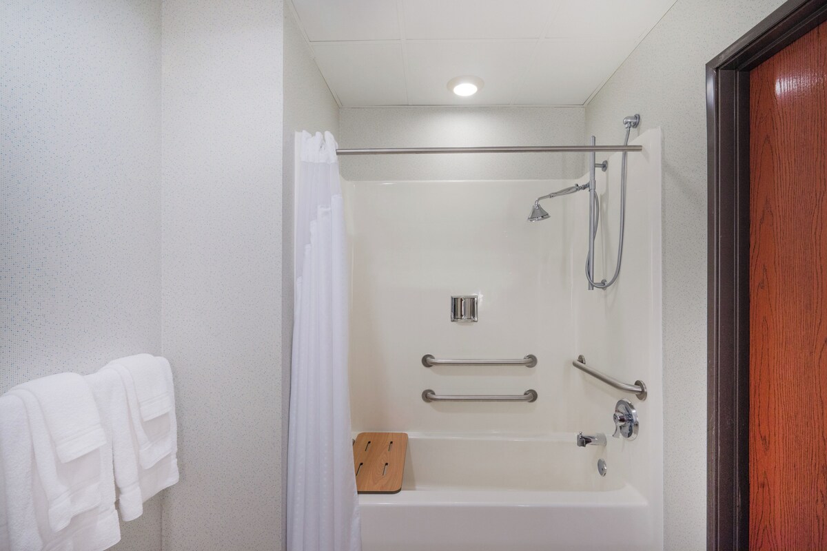 A modern bathroom with a shower, grab bars, and a wooden bath mat.