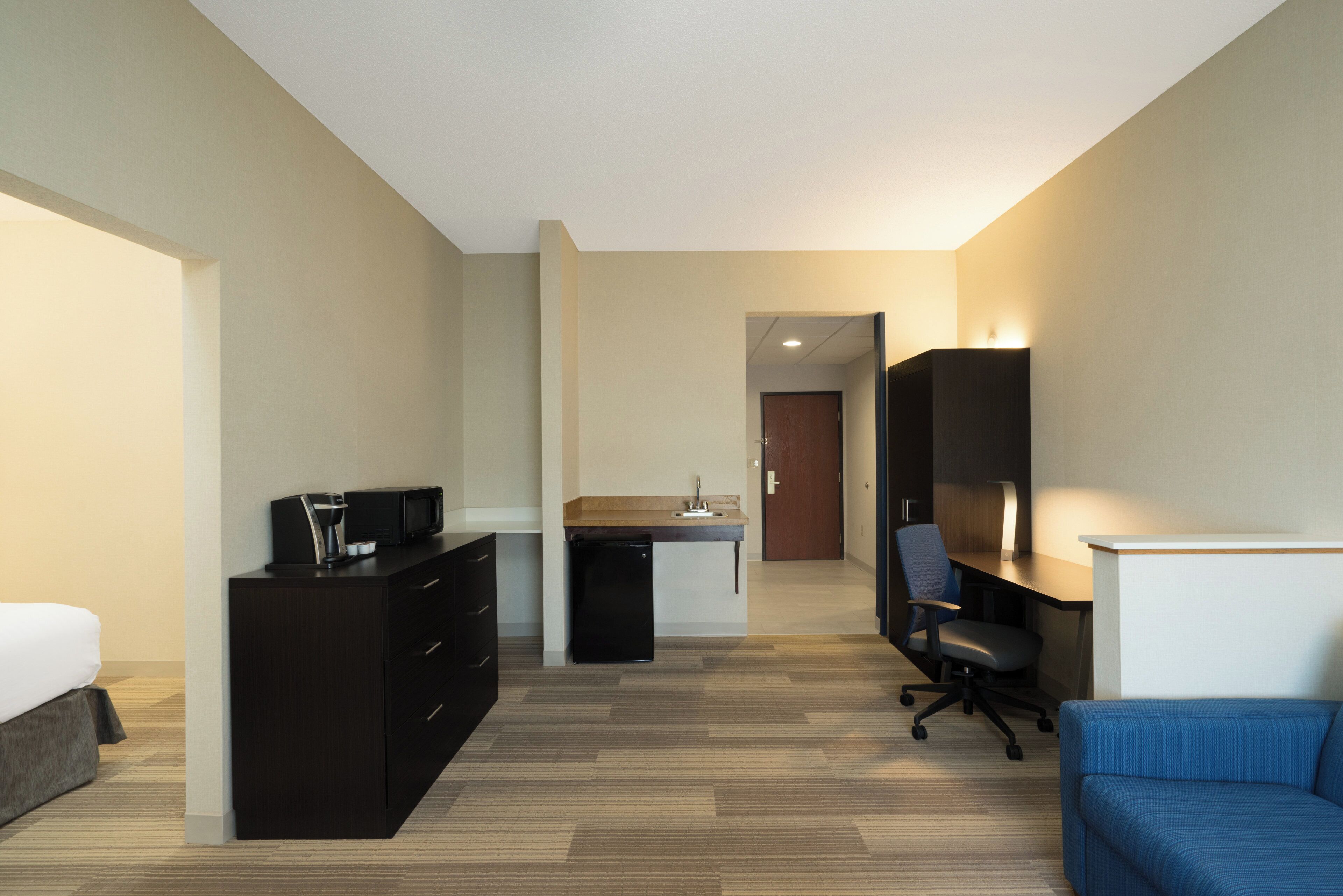 A hotel room with a bed, a desk with a chair, a kitchenette, and a bathroom.