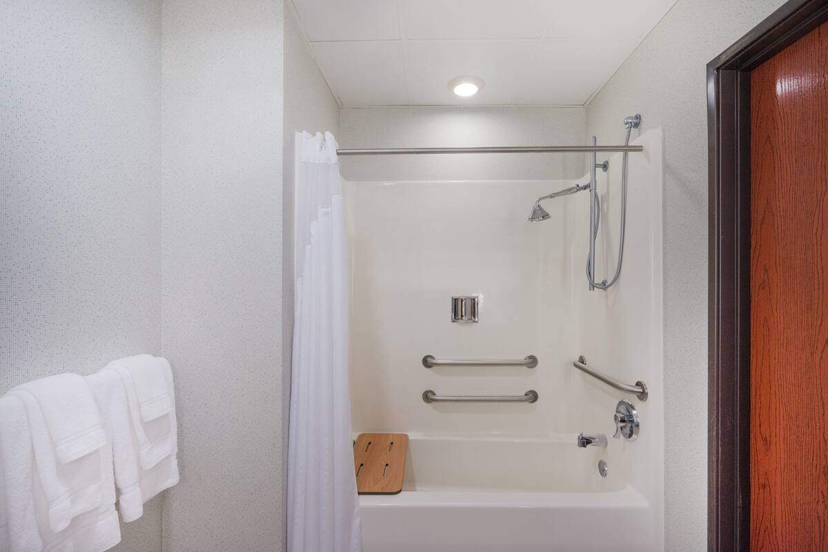 Un baño moderno con ducha, barras de apoyo y una alfombra de baño de madera.